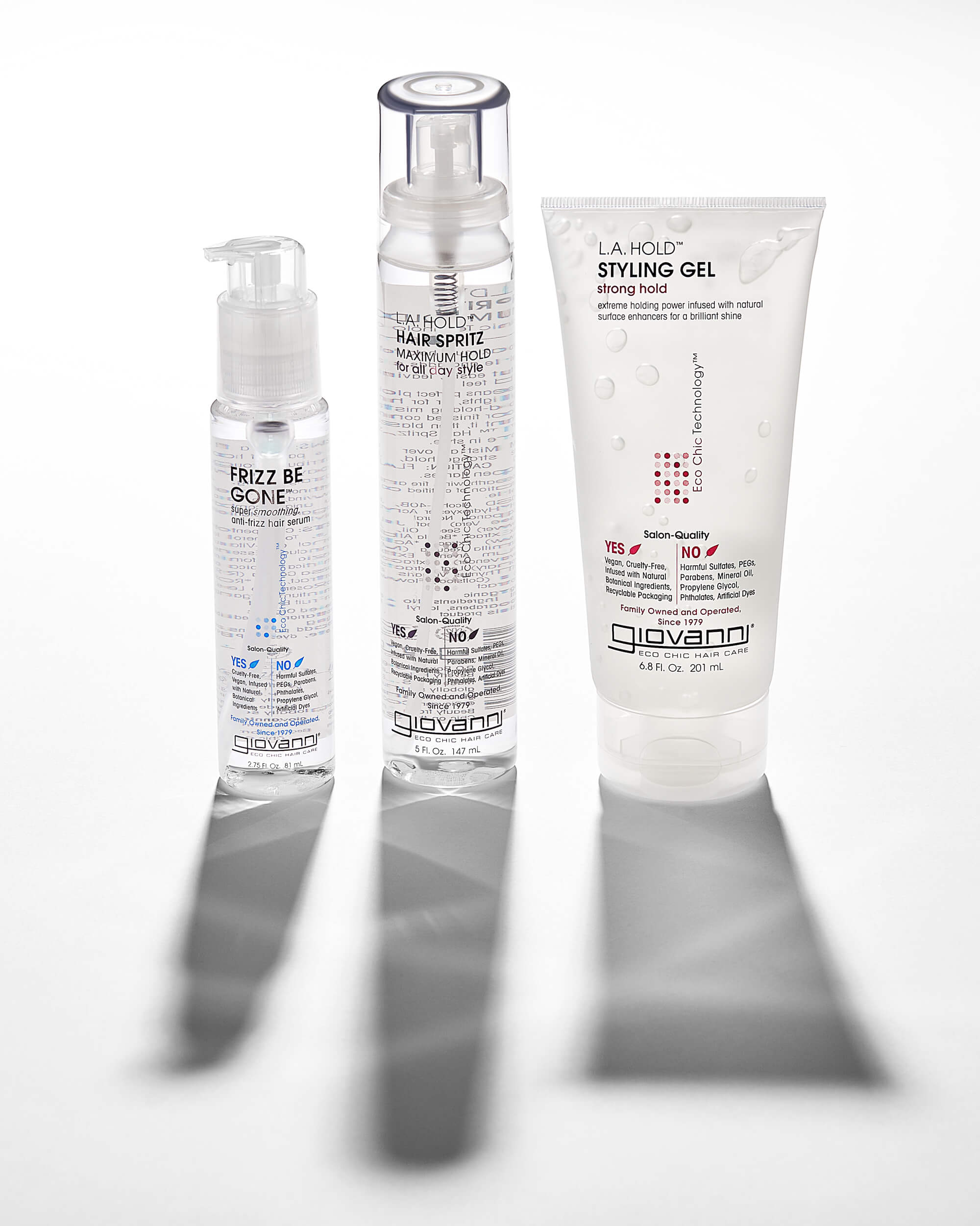 Three clear bottles of Giovanni hair products—Frizz Be Gone serum, L.A. Hold Hair Spritz, and L.A. Hold Styling Gel—stand upright on a white background with light shadows.