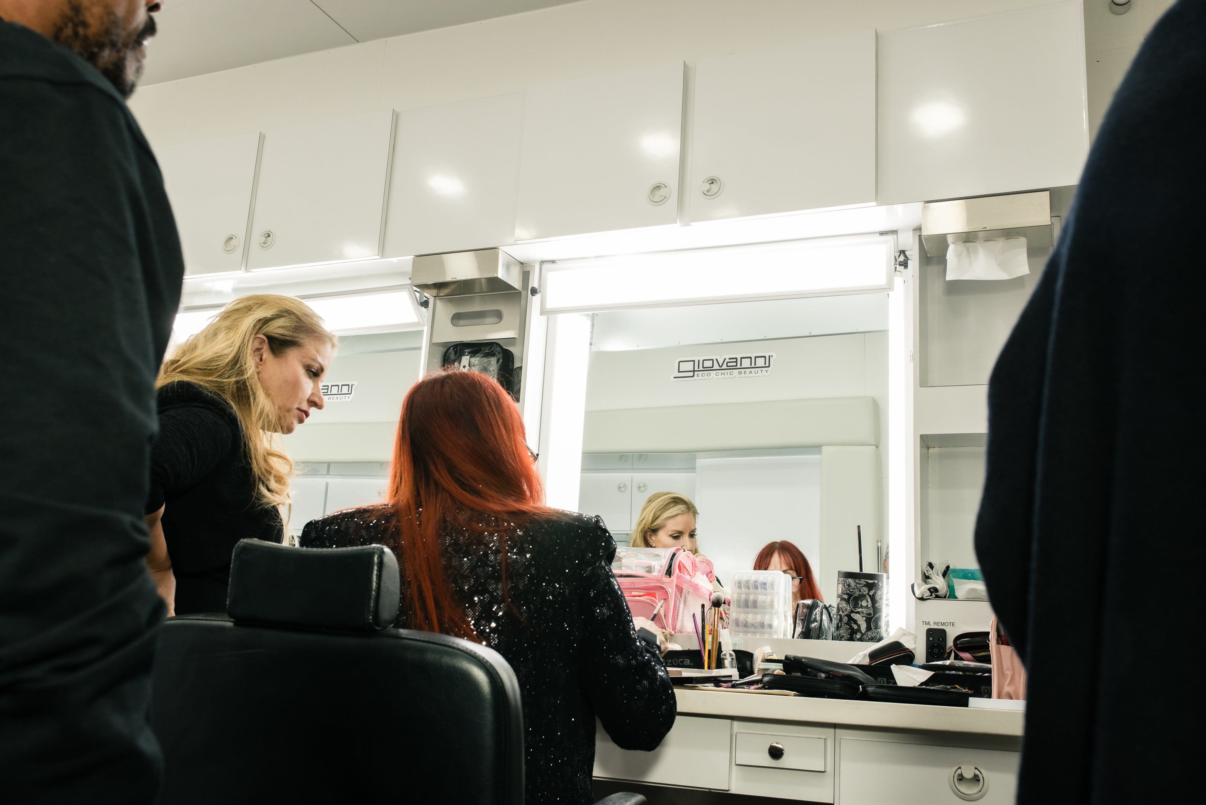 People in a beauty salon with mirrors and products on the counter.