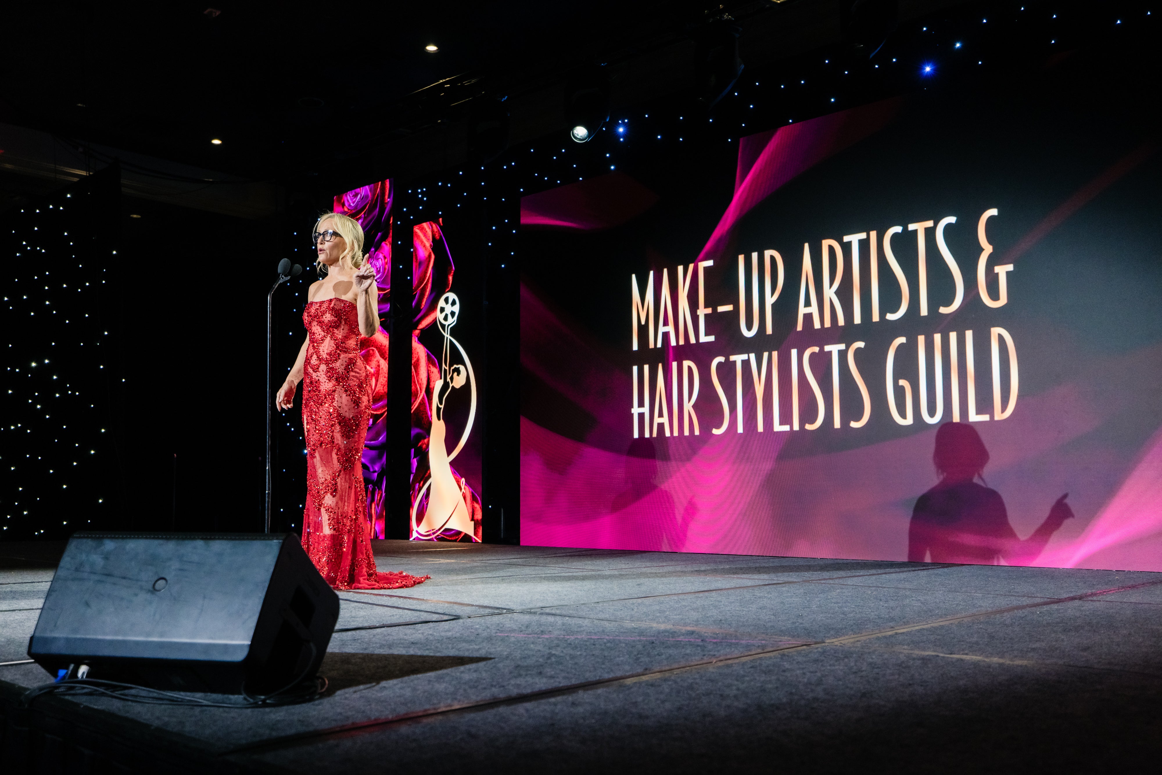 Woman in a red dress on stage at the Make-Up Artists & Hair Stylists Guild event.
