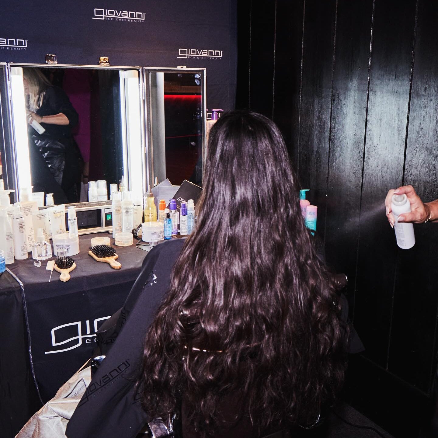 Person with long hair sitting in a chair at  a styling station with mirrors and Giovanni products.