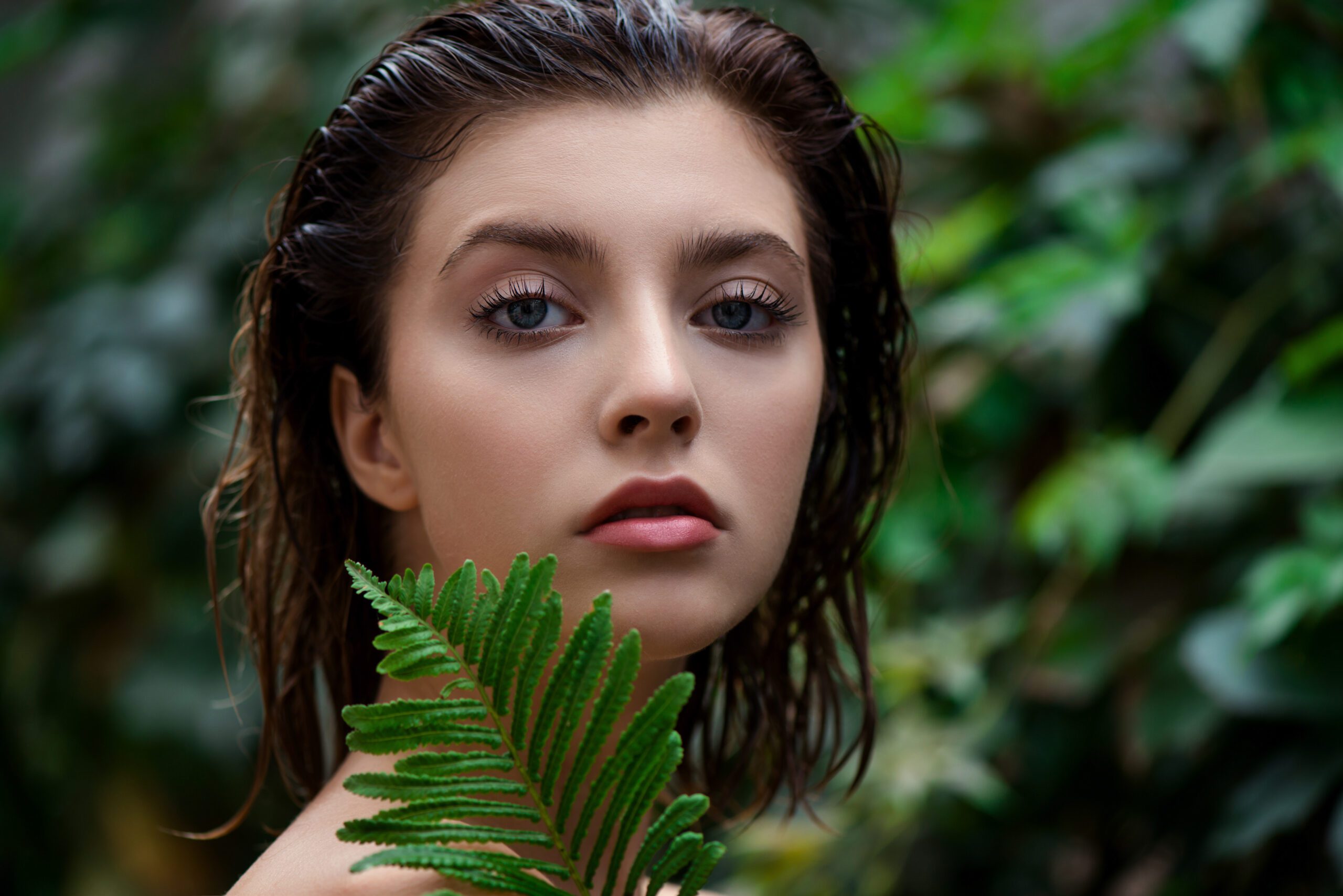 Woman with wet hair, holding a green fern leaf, surrounded by lush foliage