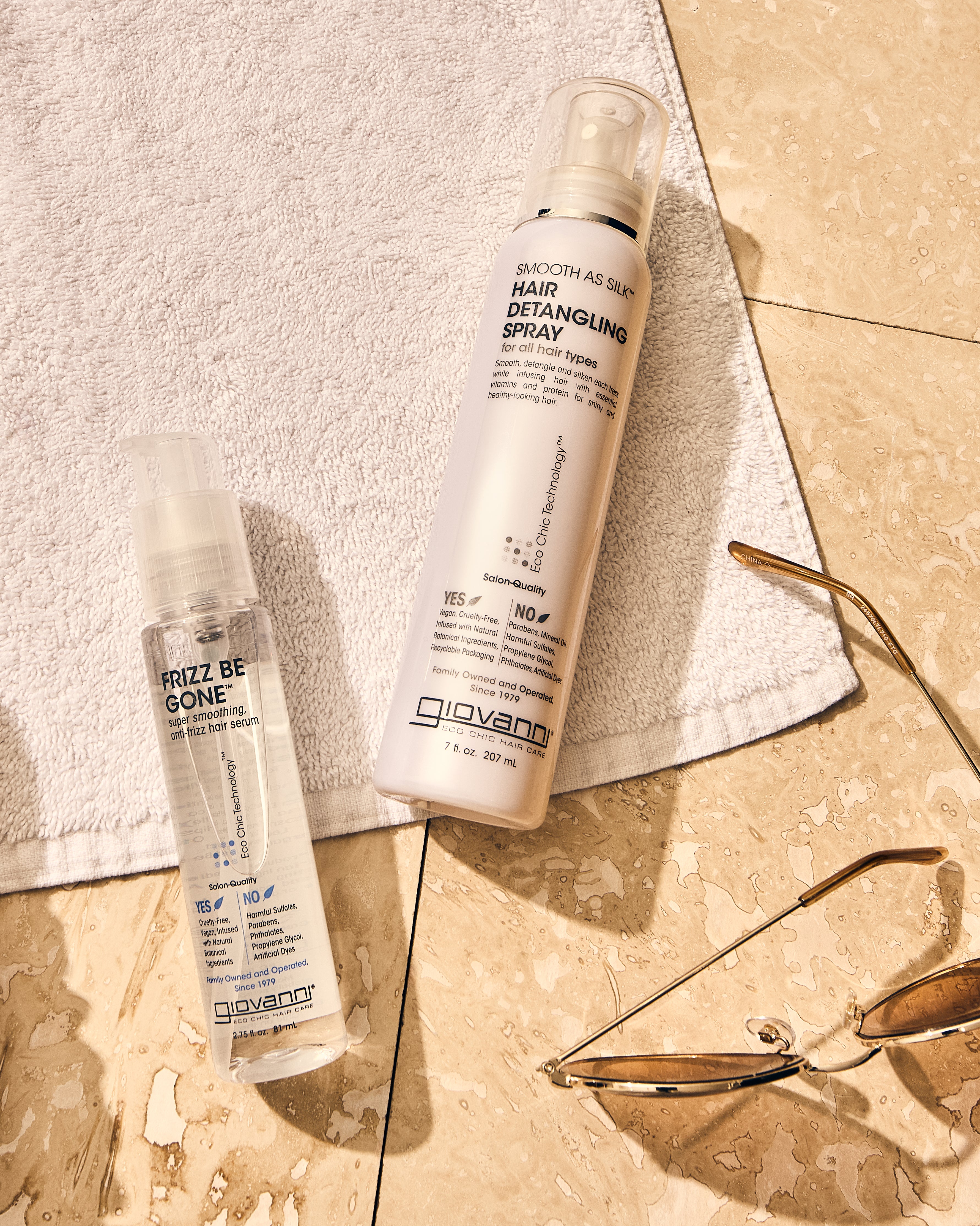 Image of Smooth As Silk Hair Detangling Spray and Frizz Be Gone Hair Serum laying on a towel on top of bathroom vanity tile. 