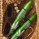 Hemp Hydrating Leave-In Conditioning & Styling Elixir and Hair Serum bottles nestled in raffia basket with sunglasses and gold hair clip.