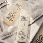 Bottles of Tea Tree Triple Treat Shampoo and Conditioner laying on crisp white bath robe.