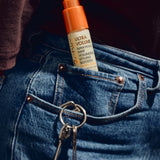 A bottle of ULTRA VOLUME Super Potion Hair Volumizing Styling Booster tucked into the pocket of blue jeans next to keys.