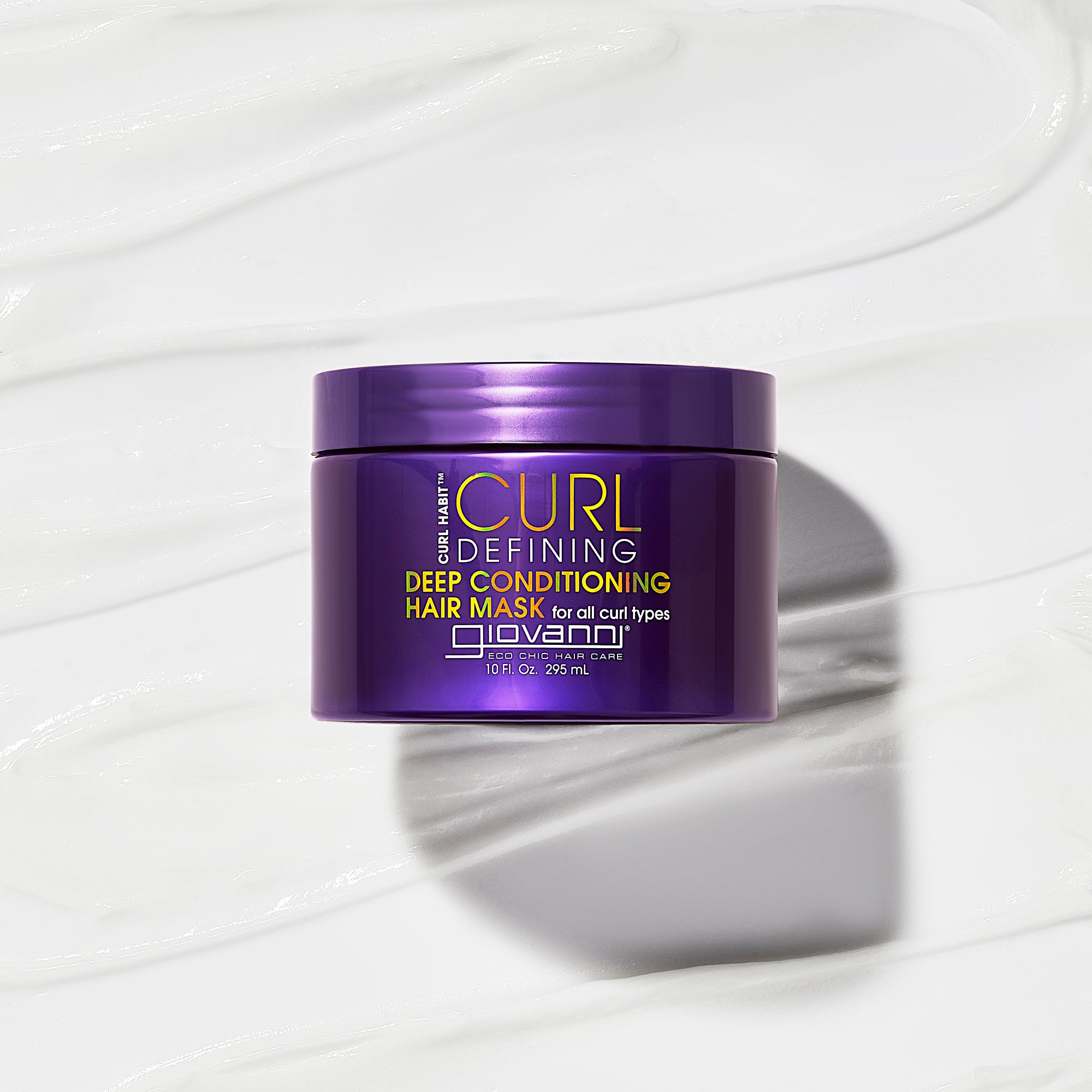 A purple container of Giovanni Cosmetics CURL HABIT™ CURL DEFINING DEEP CONDITIONING HAIR MASK sits on a creamy white background, highlighting its hydrating, curl-enhancing, and moisturizing formula.