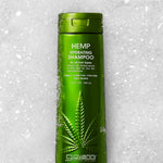A green bottle of Giovanni Cosmetics HEMP HYDRATING SHAMPOO - 3 Sizes rests on snow and ice, featuring a large hemp leaf and bold vegan hair care details in white and yellow text on the front label.