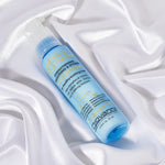 A blue bottle of Giovanni Cosmetics BIOTIN & COLLAGEN STRENGTHENING SMOOTHING & STYLING HAIR SERUM with a pump dispenser rests on white satin, featuring yellow and blue label text for boosting hair volume.