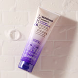 A tube of Giovanni Cosmetics 2chic® REPAIRING SHAMPOO rests on wet white tiles. The white-to-purple packaging displays blackberry and coconut milk for damaged hair, with water droplets visible near this repairing shampoo.