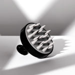 The Giovanni Cosmetics SCALP MASSAGER & SHAMPOO BRUSH (Black Handle) features pointed silicone bristles and sits on a white surface, casting geometric shadows—a salon-quality tool ideal for natural hair care.