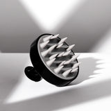 The Giovanni Cosmetics SCALP MASSAGER & SHAMPOO BRUSH (Black Handle) features pointed silicone bristles and sits on a white surface, casting geometric shadows—a salon-quality tool ideal for natural hair care.