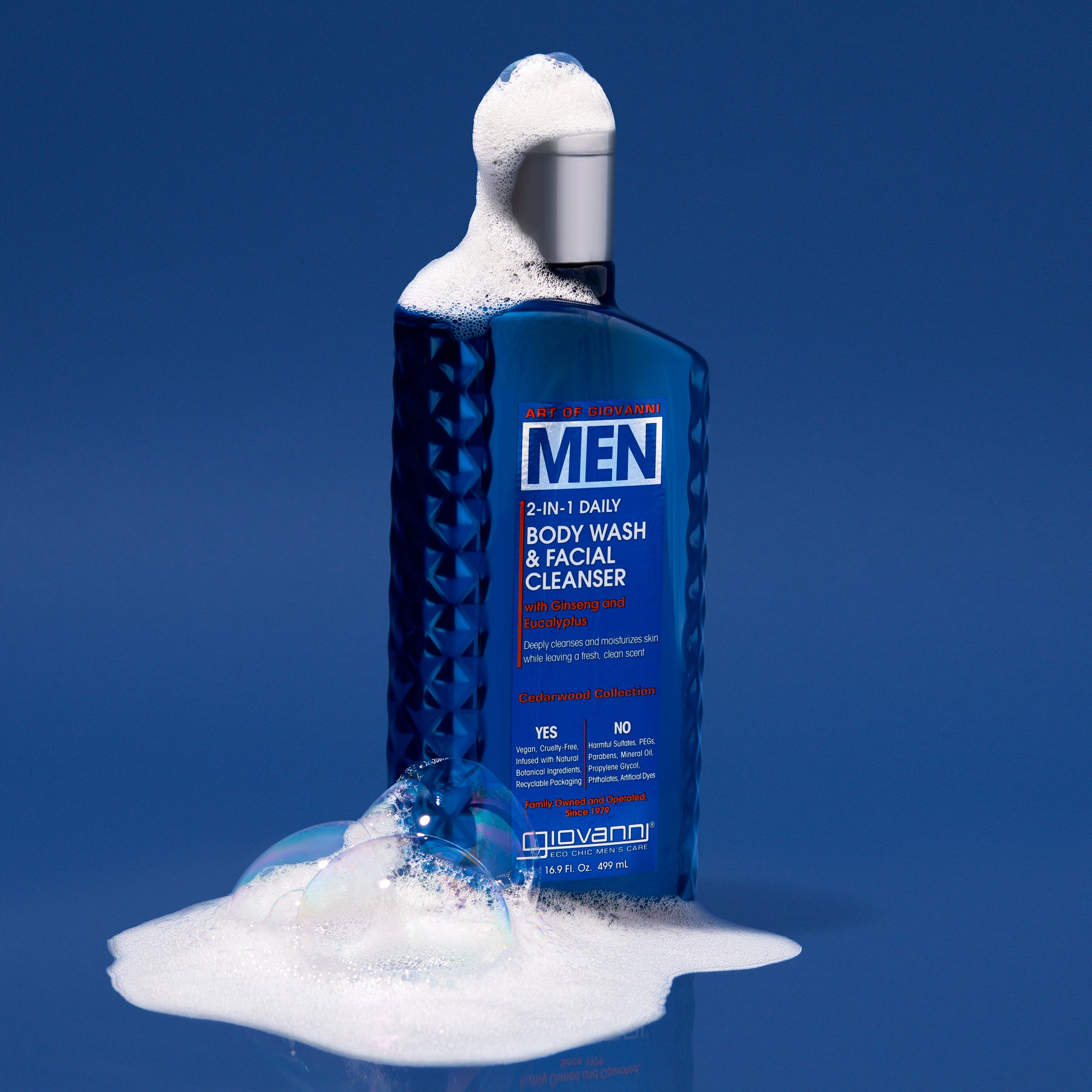A blue bottle of Giovanni Cosmetics MEN 2-in-1 Daily Body Wash & Facial Cleanser with Ginseng & Eucalyptus stands upright with suds and bubbles on its cap and base, set against a solid blue background.