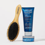 A wooden hairbrush with black bristles stands beside a blue tube of Giovanni Cosmetics MEN Strong Hold Hair Styling Gel with Ginseng and Eucalyptus, plus a small blue jar of styling clay, set against a white background.