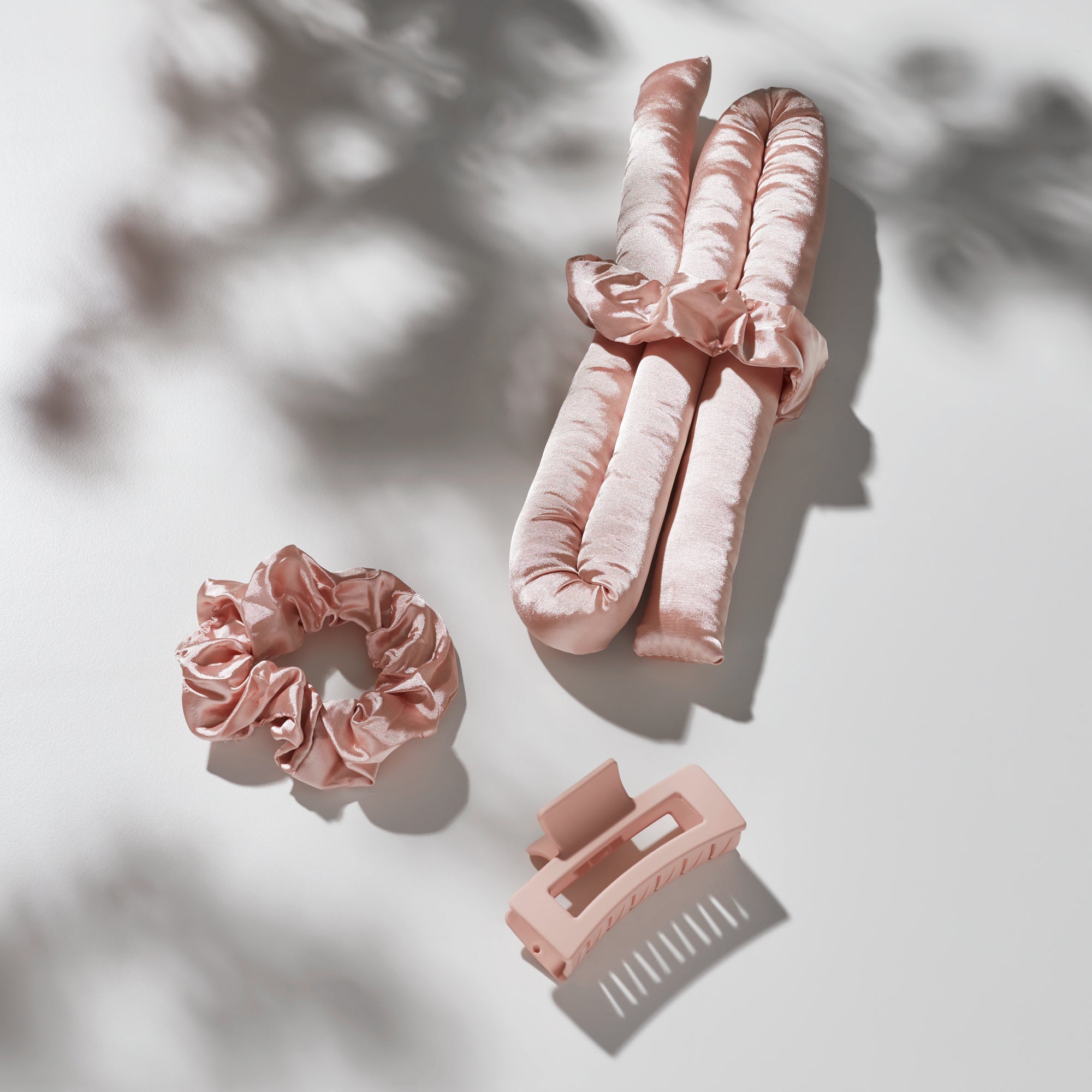 The Giovanni Cosmetics HEATLESS SATIN HAIR CURLING SET (blush) includes two satin curling rods, two matching scrunchies, and a pink hair clip—all elegantly arranged on a light surface with soft shadows for effortless, frizz-free curls.