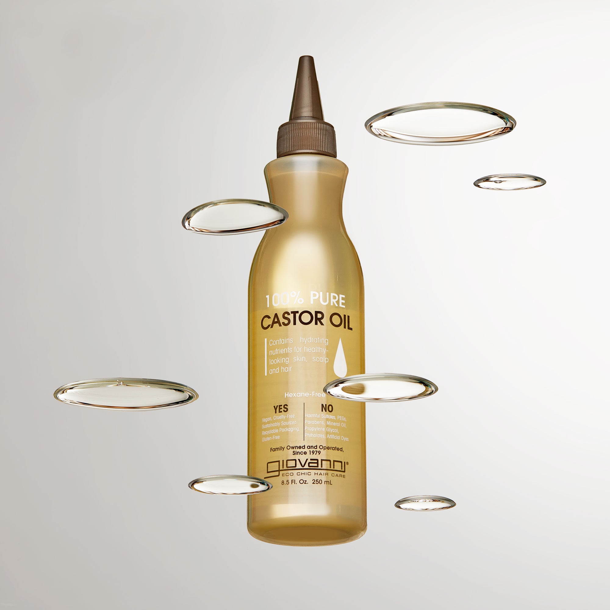 A bottle of Giovanni Cosmetics SMOOTHING CASTOR OIL with a pointed nozzle is surrounded by oil drops on a light background—ideal for naturally moisturizing and nourishing hair.