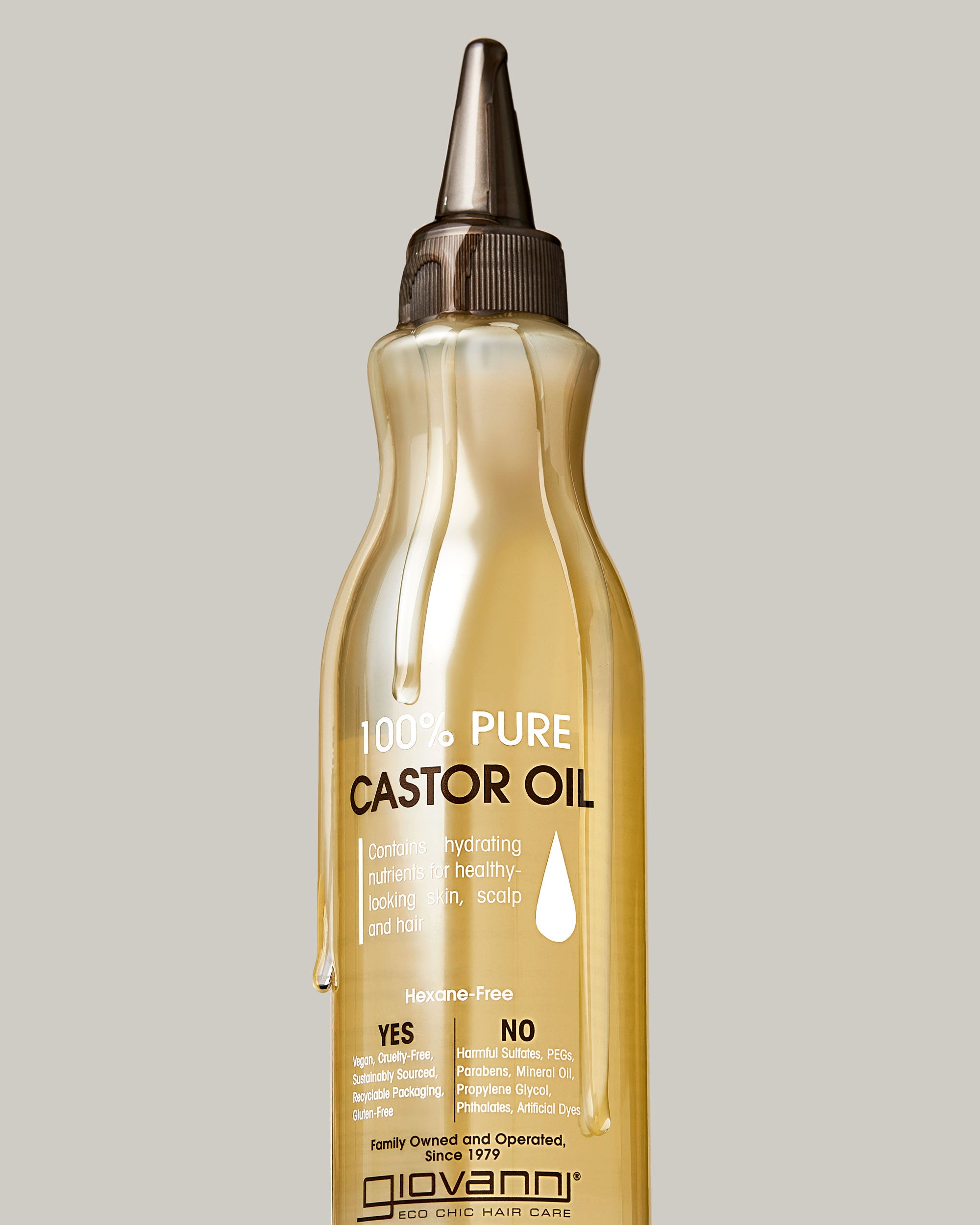 A clear bottle of Giovanni Cosmetics SMOOTHING CASTOR OIL with a pointed applicator cap and labeled details, showing oil drips on the outside, ideal for hair treatment or moisturizing, set against a plain light gray background.