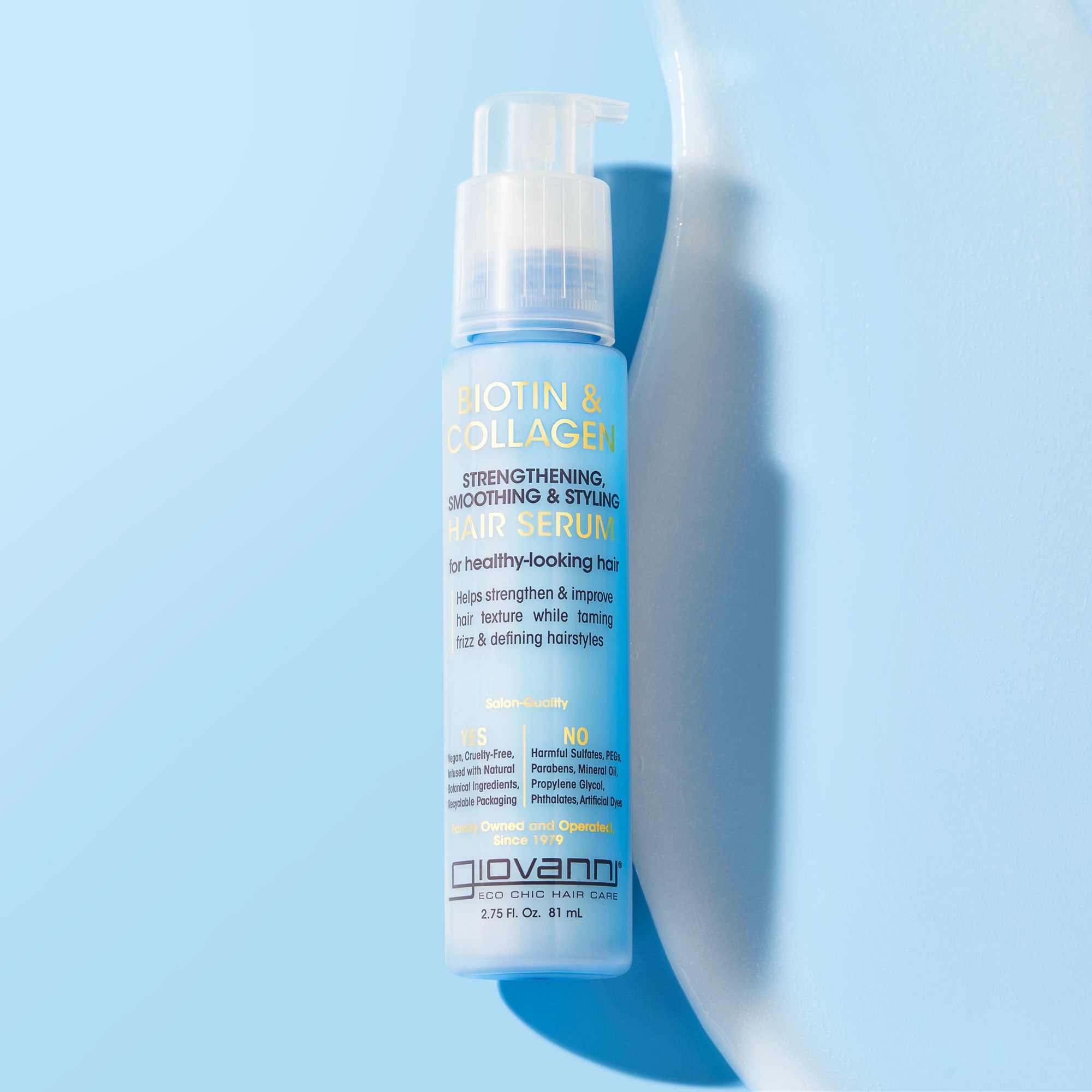 A bottle of Giovanni Cosmetics BIOTIN & COLLAGEN STRENGTHENING SMOOTHING & STYLING HAIR SERUM stands upright on a light blue surface with a curved white accent, its label promoting stronger, smoother hair with added volume.