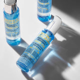 Three blue bottles of Giovanni Cosmetics BIOTIN & COLLAGEN REBONDING & RESTORING HAIR OIL are displayed on a light surface—one lying down and two standing upright—highlighting their volumizing formula and soft shadows.