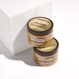 Two jars of Giovanni Cosmetics SMOOTHING CASTOR OIL STRENGTHENING HAIR MASK, in gold packaging with black lids and white text, sit stacked on a white surface—luxuriously hydrating and strengthening dry, damaged hair.