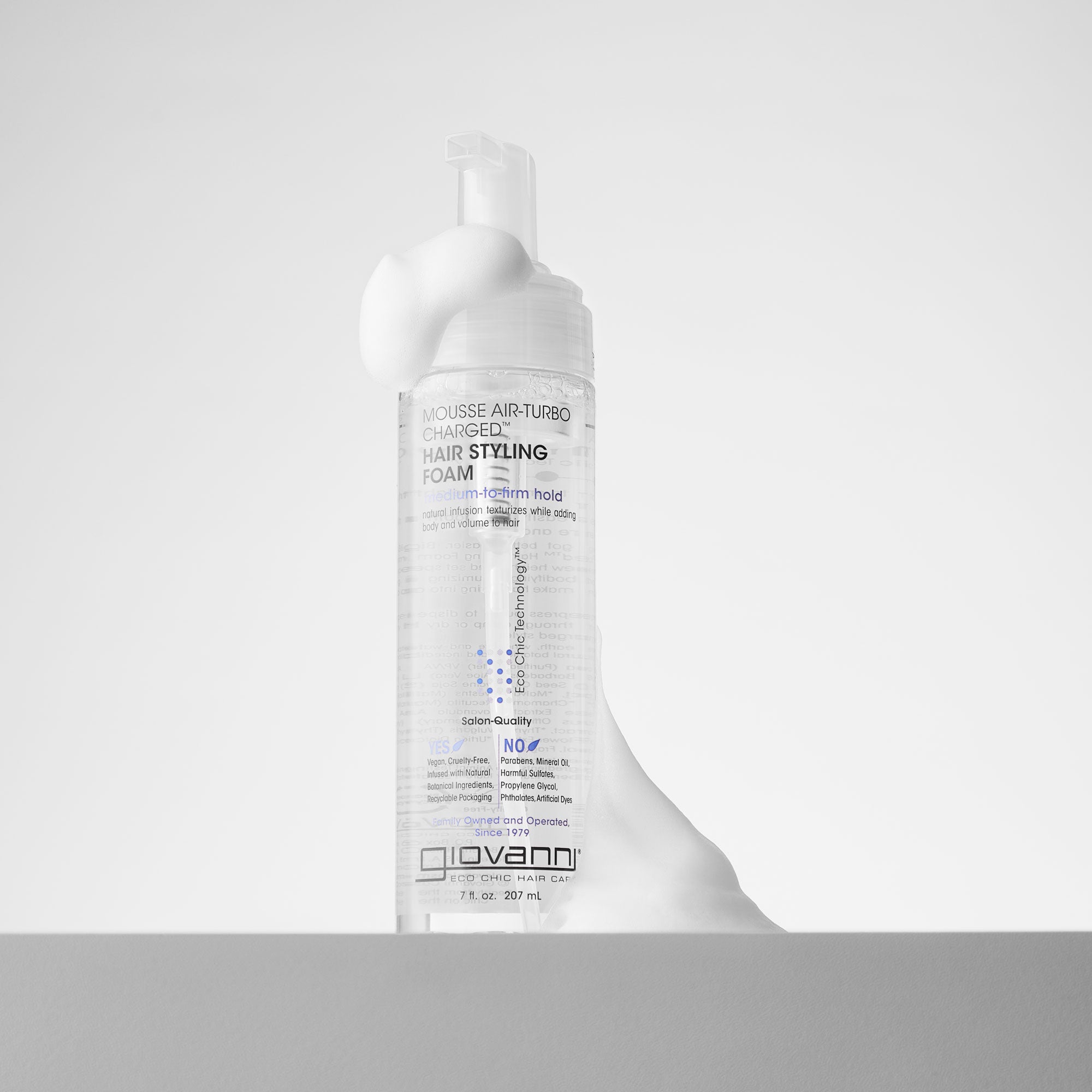 A clear bottle of Giovanni Cosmetics MOUSSE AIR-TURBO CHARGED™ HAIR STYLING FOAM with white mousse overflowing from the pump, set against a plain white background.