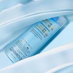 A blue bottle of Giovanni Cosmetics BIOTIN & COLLAGEN LEAVE-IN CONDITIONER rests on a light blue surface, with volumizing creamy conditioner artfully spread around it in smooth strokes.