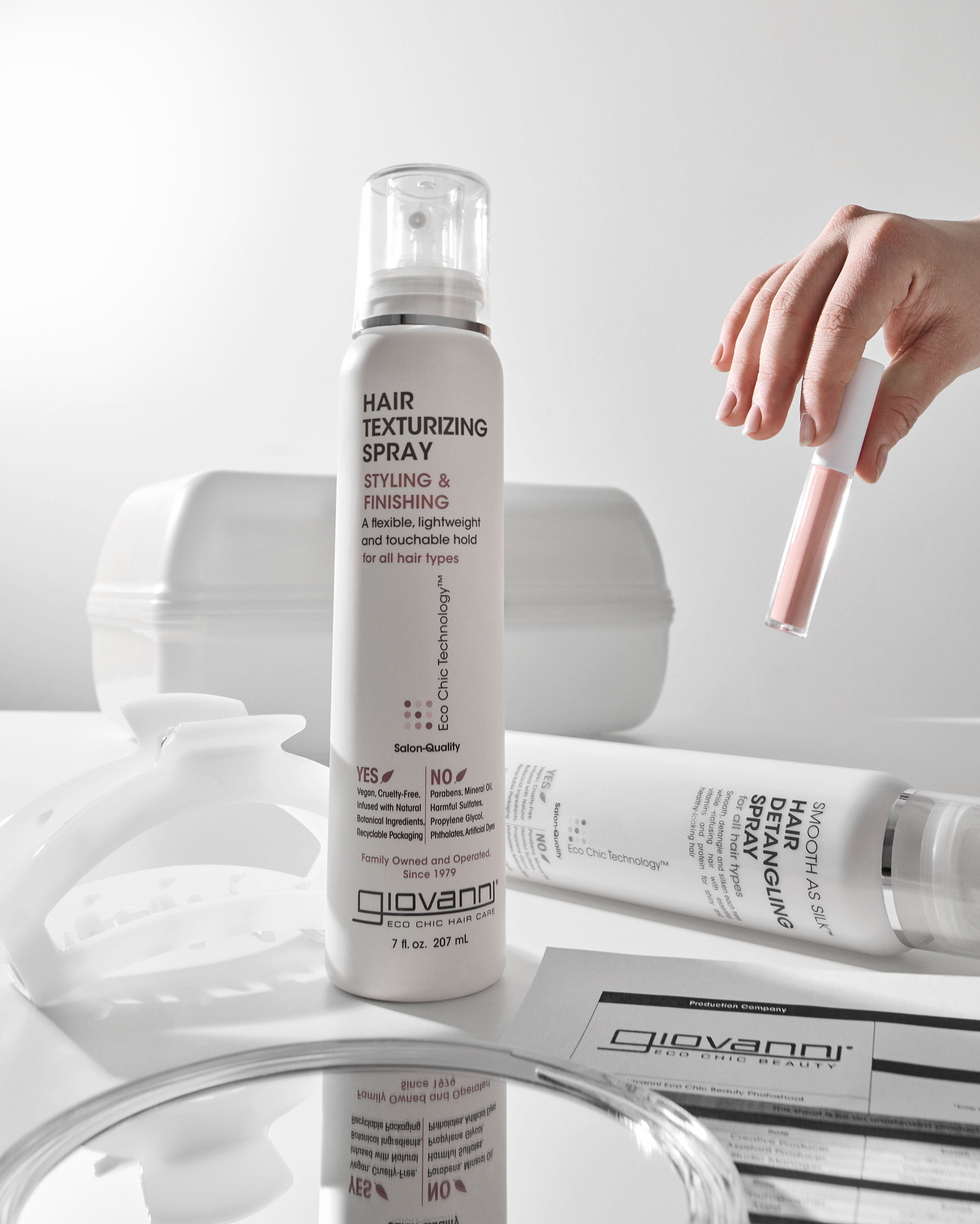 Giovanni hair texturizing spray bottle on a white surface with a hand holding a spray nozzle.