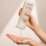 Hand holding a bottle of Giovanni Root 66 Max Volume Shampoo against a neutral background