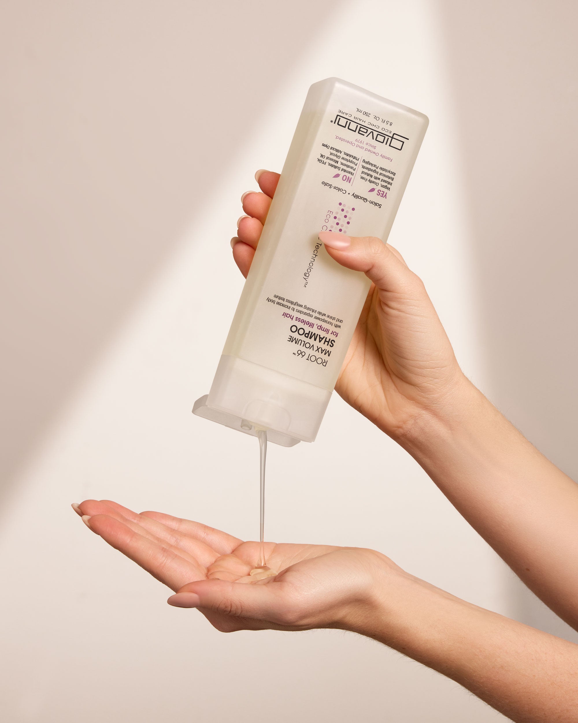 Hand holding a bottle of Giovanni Root 66 Max Volume Shampoo against a neutral background