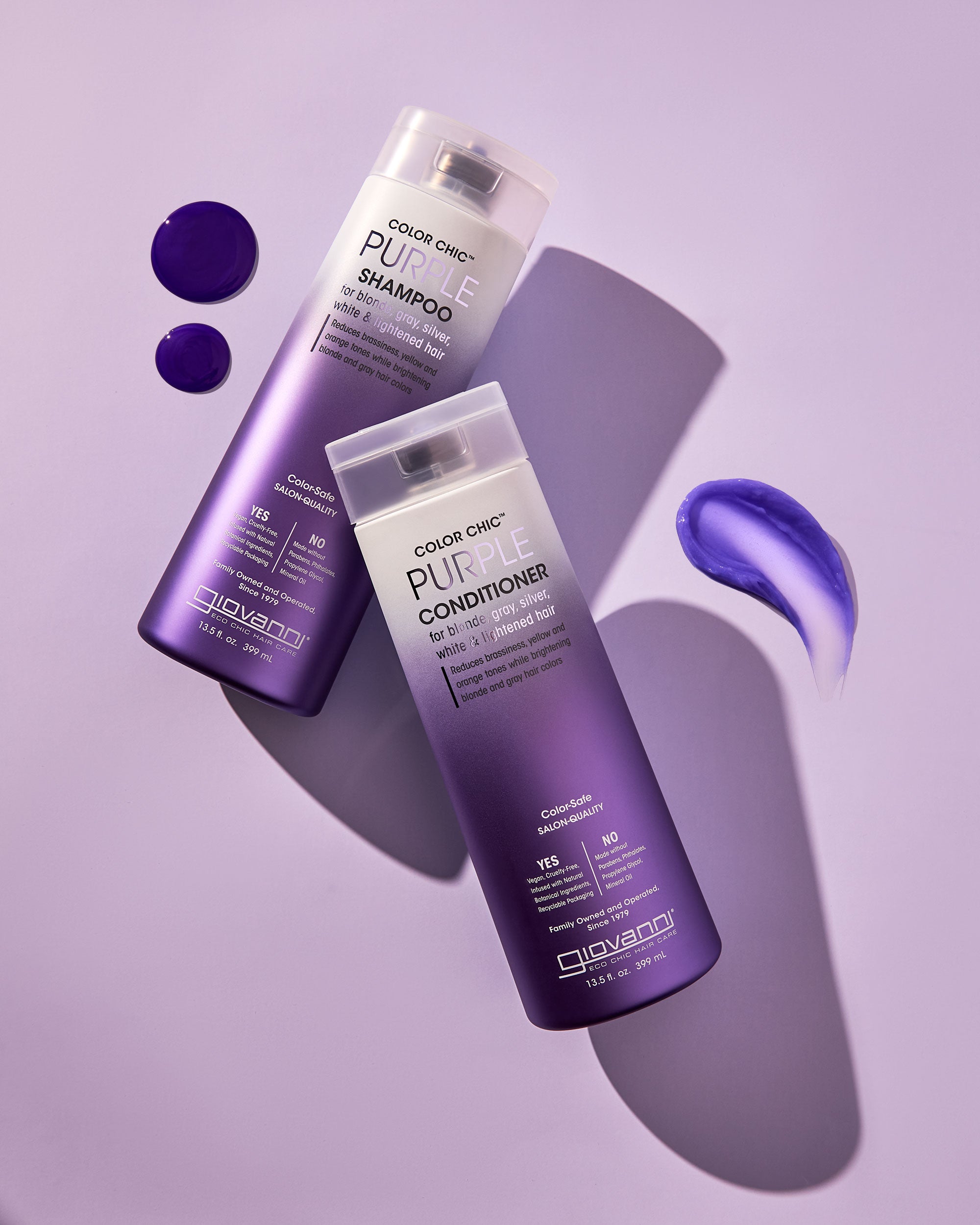 A bottle of Giovanni Cosmetics COLOR CHIC™ PURPLE CONDITIONER rests on a purple surface with conditioner swatches nearby—ideal for enhancing blonde tones or maintaining silver hair, all styled in soft, angled lighting.