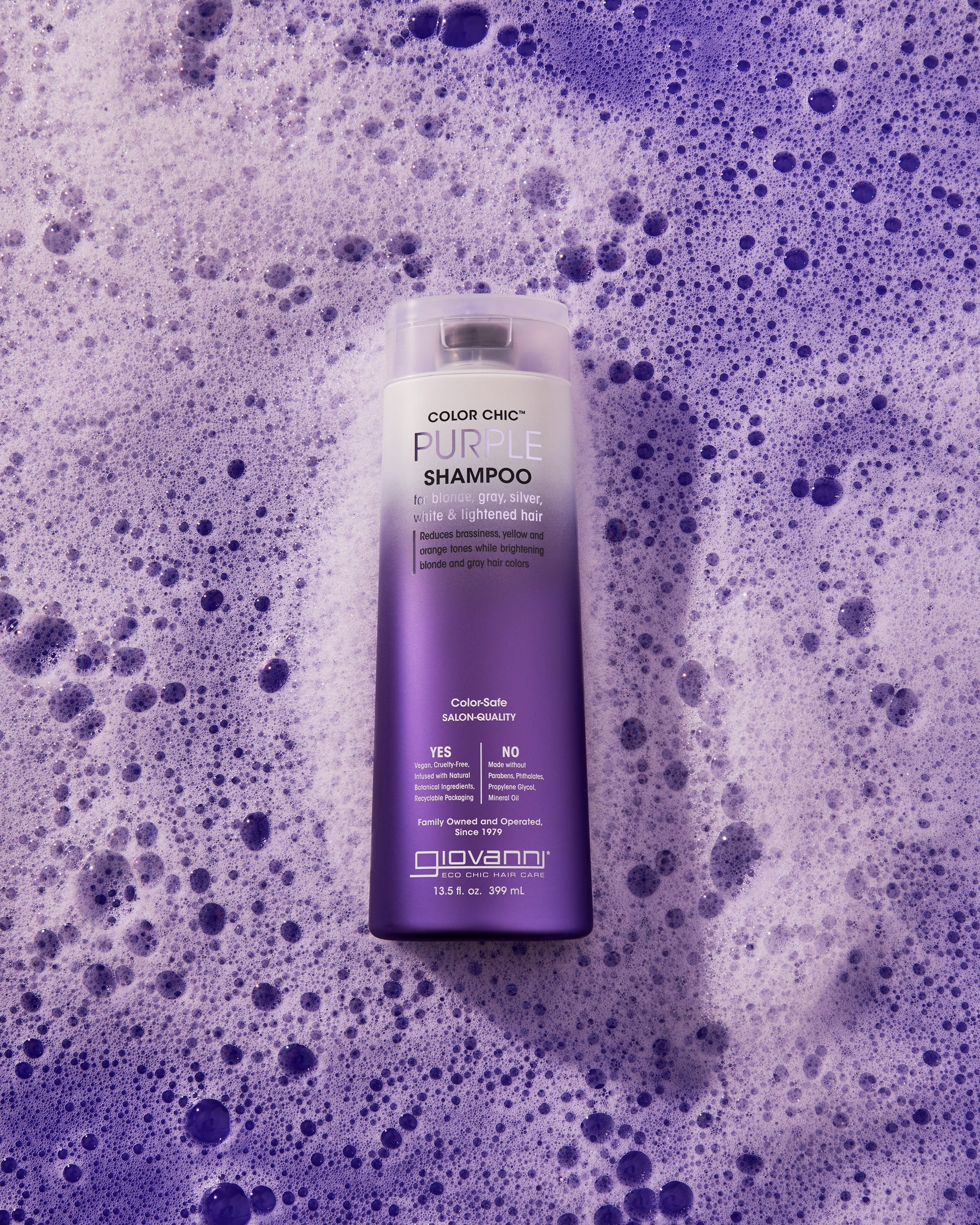 A bottle of Giovanni Cosmetics COLOR CHIC™ PURPLE SHAMPOO for color-treated, lightened hair sits on purple foam. The white-to-purple bottle helps reduce brassy tones in blonde hair.
