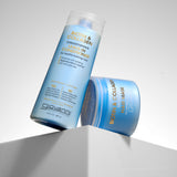 Two blue Giovanni Cosmetics BIOTIN & COLLAGEN RESTORING HAIR MASKs for hair volume are displayed on a white geometric pedestal against a light gray background.