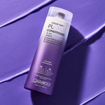 A bottle of Giovanni Cosmetics COLOR CHIC™ PURPLE CONDITIONER for blonde or silver hair stands upright on a textured purple surface, with matching conditioner streaks nearby and the label clearly visible.