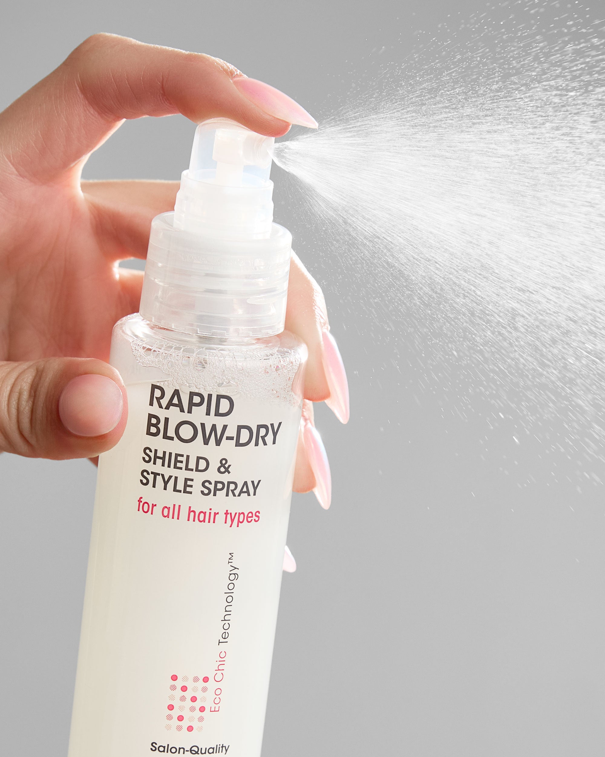 Hand holding a bottle of Giovanni Rapid Blow-Dry Shield & Style Spray with a gray background