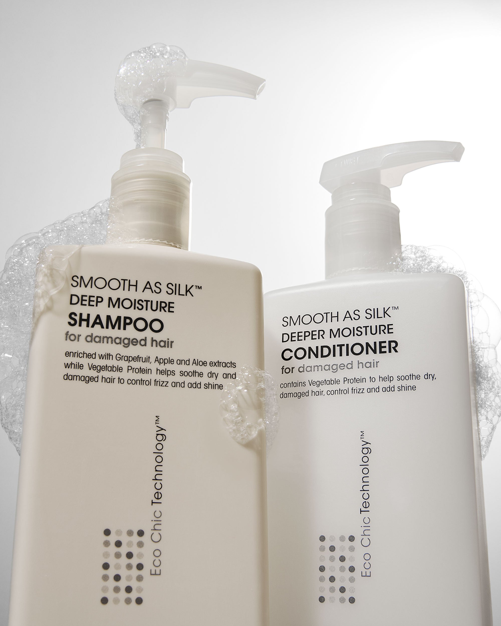 Two white pump bottles of Giovanni Cosmetics SMOOTH AS SILK™ DEEPER MOISTURE CONDITIONER, labeled for damaged hair, offer color-safe, silky hydration and appear with bubbles on top against a light background.