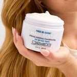 Hand holding a jar of Giovanni Frizz Be Gone hair mask with blonde hair in the background