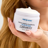 Hand holding a jar of Giovanni Frizz Be Gone hair mask with blonde hair in the background
