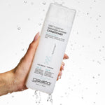 Hand holding a bottle of Giovanni Direct Leave-In Weightless Moisture Conditioner with water droplets in the background.