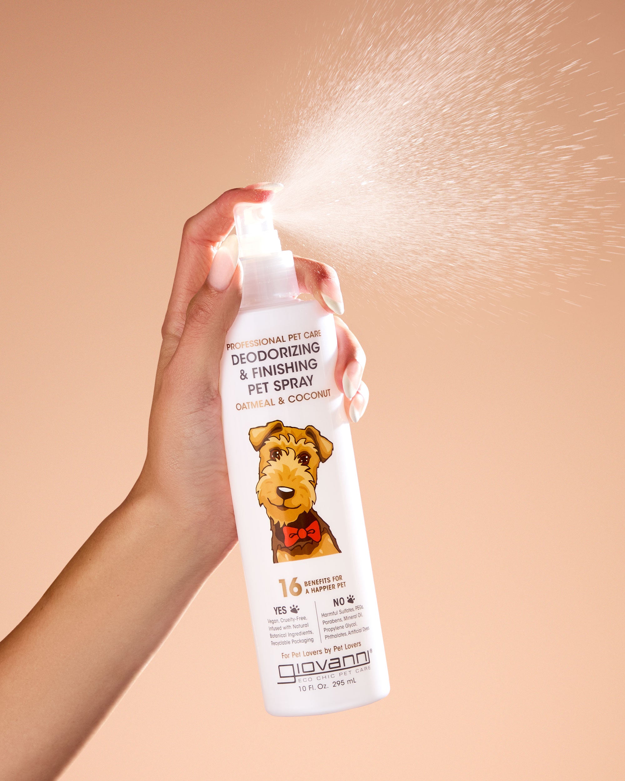 Hand holding a bottle of Giovanni pet spray on a beige background