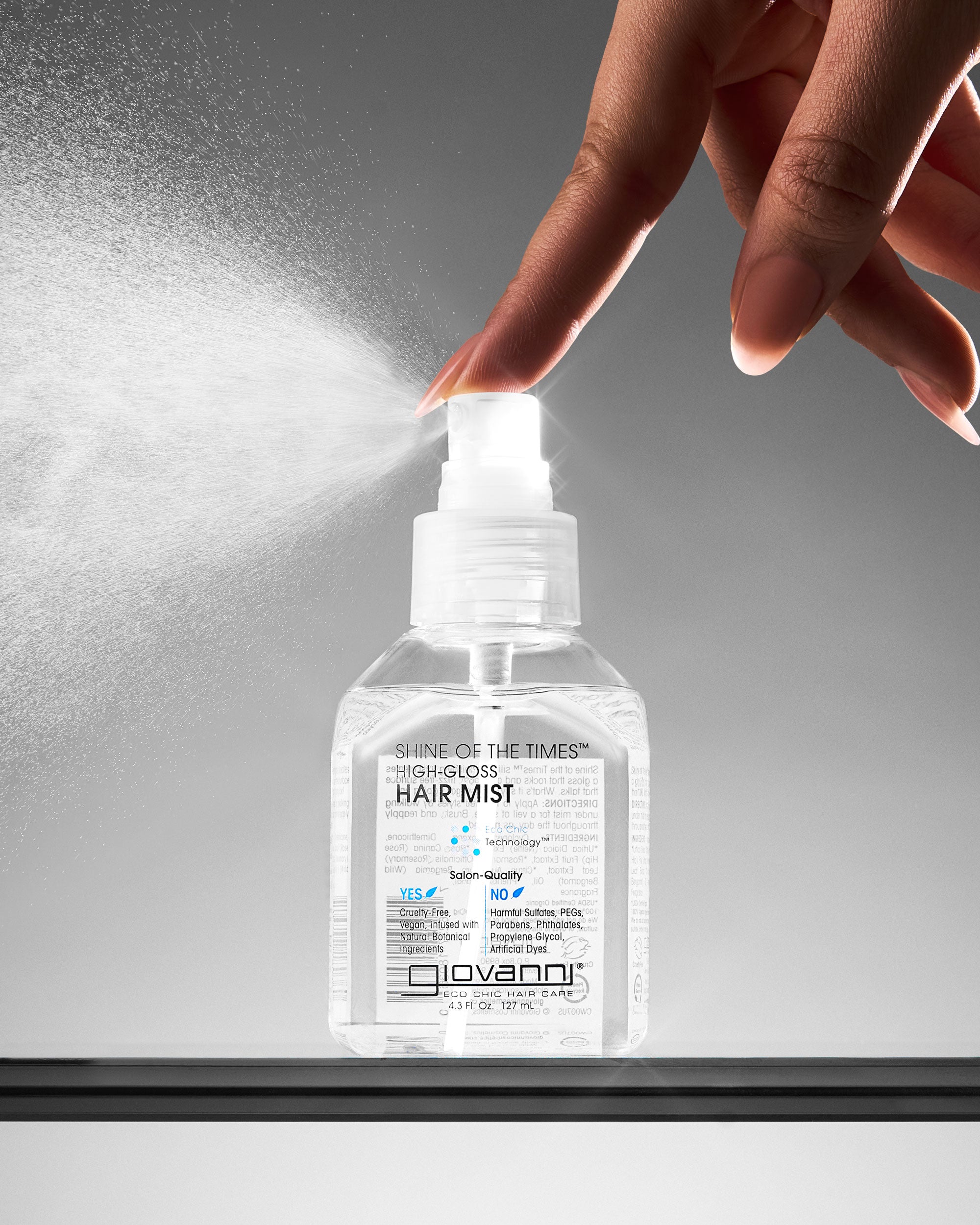 Bottle of Giovanni High-Gloss Hair Mist being sprayed with a hand against a gray background