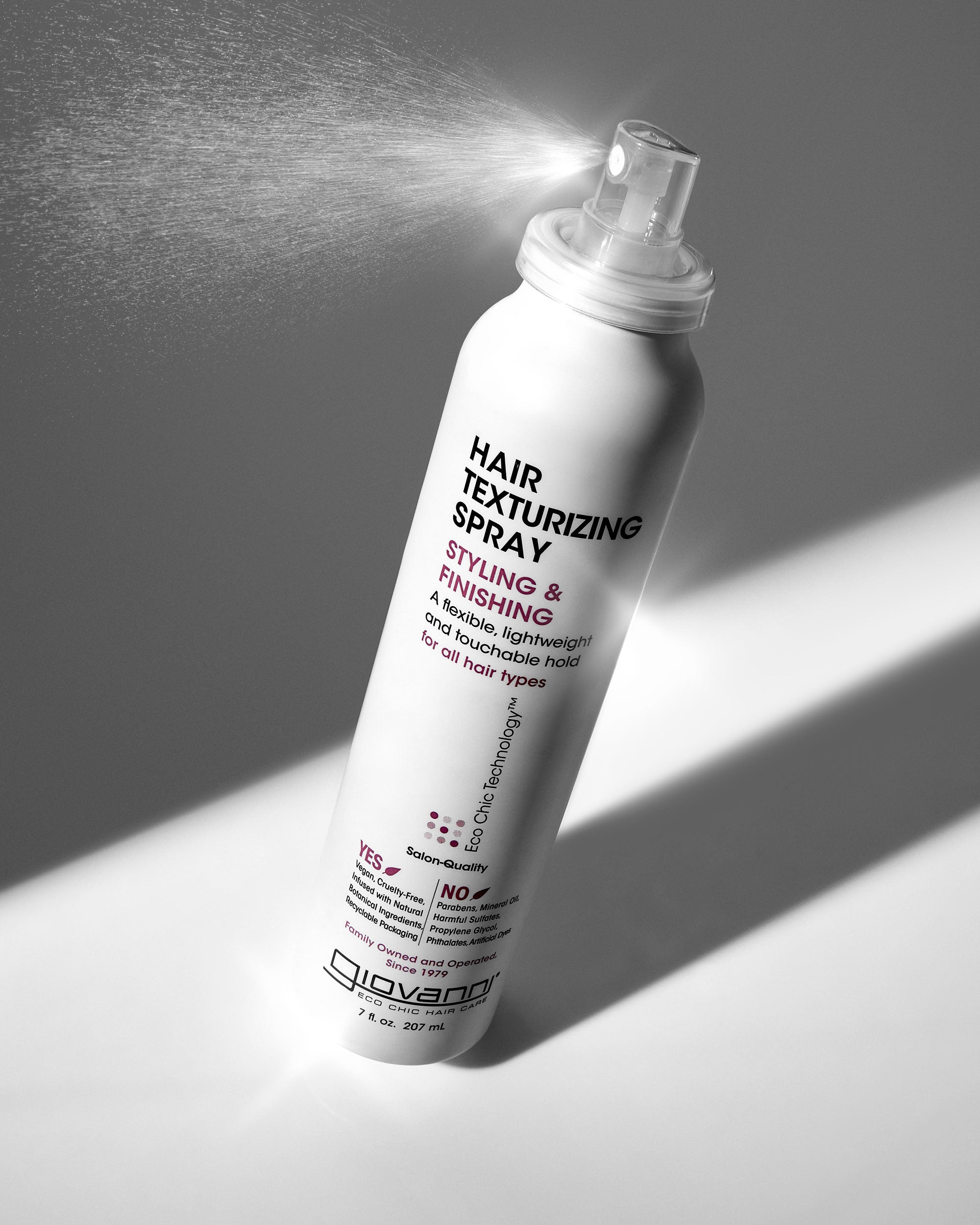 Giovanni Hair texturizing spray bottle with a spray action on a gray background