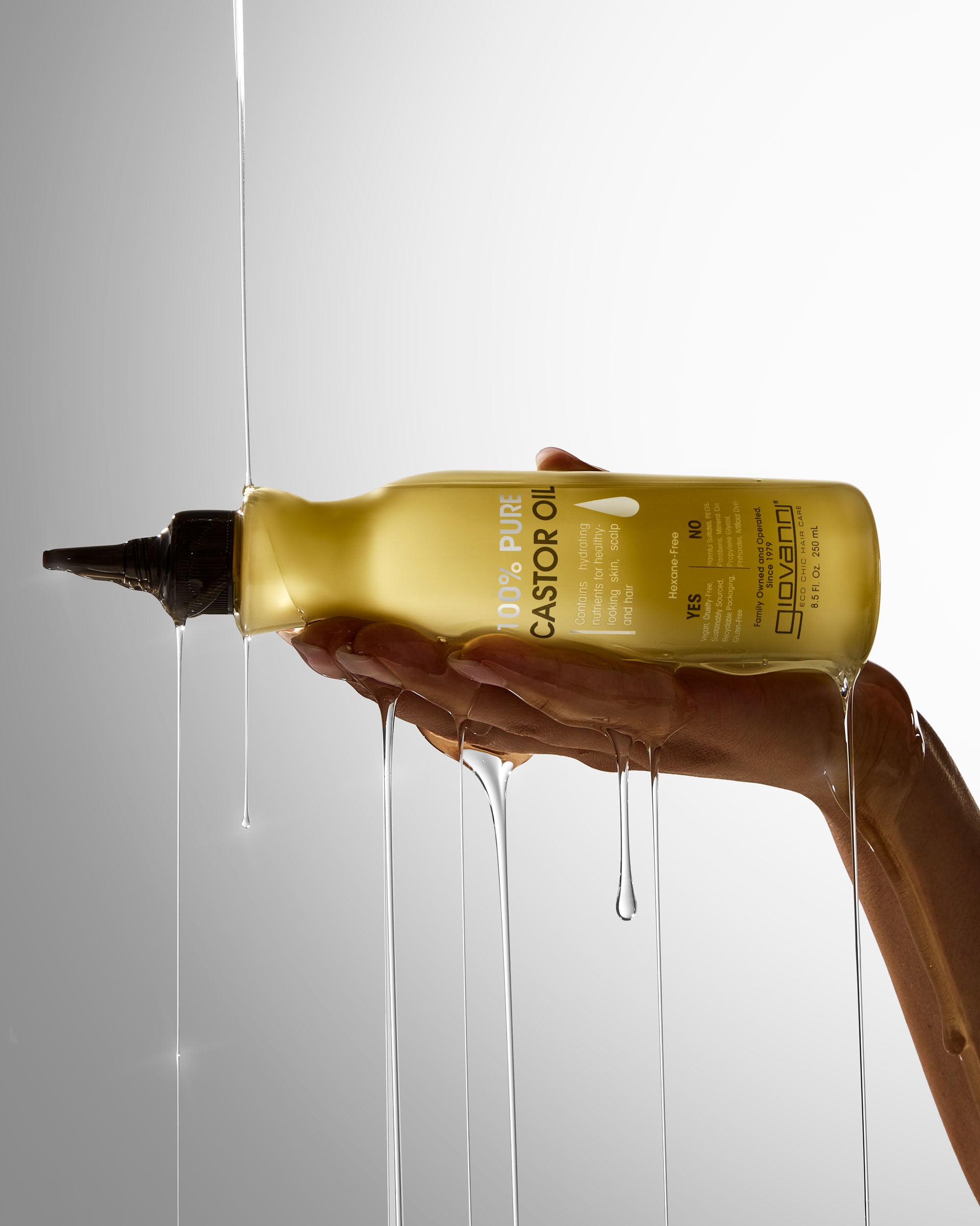 Hand holding a bottle of Giovanni Castor Oil with oil dripping