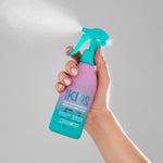 Hand holding Giovanni Eco Chic Kids Hair Smoothing & Detangling Spray bottle against a gray background