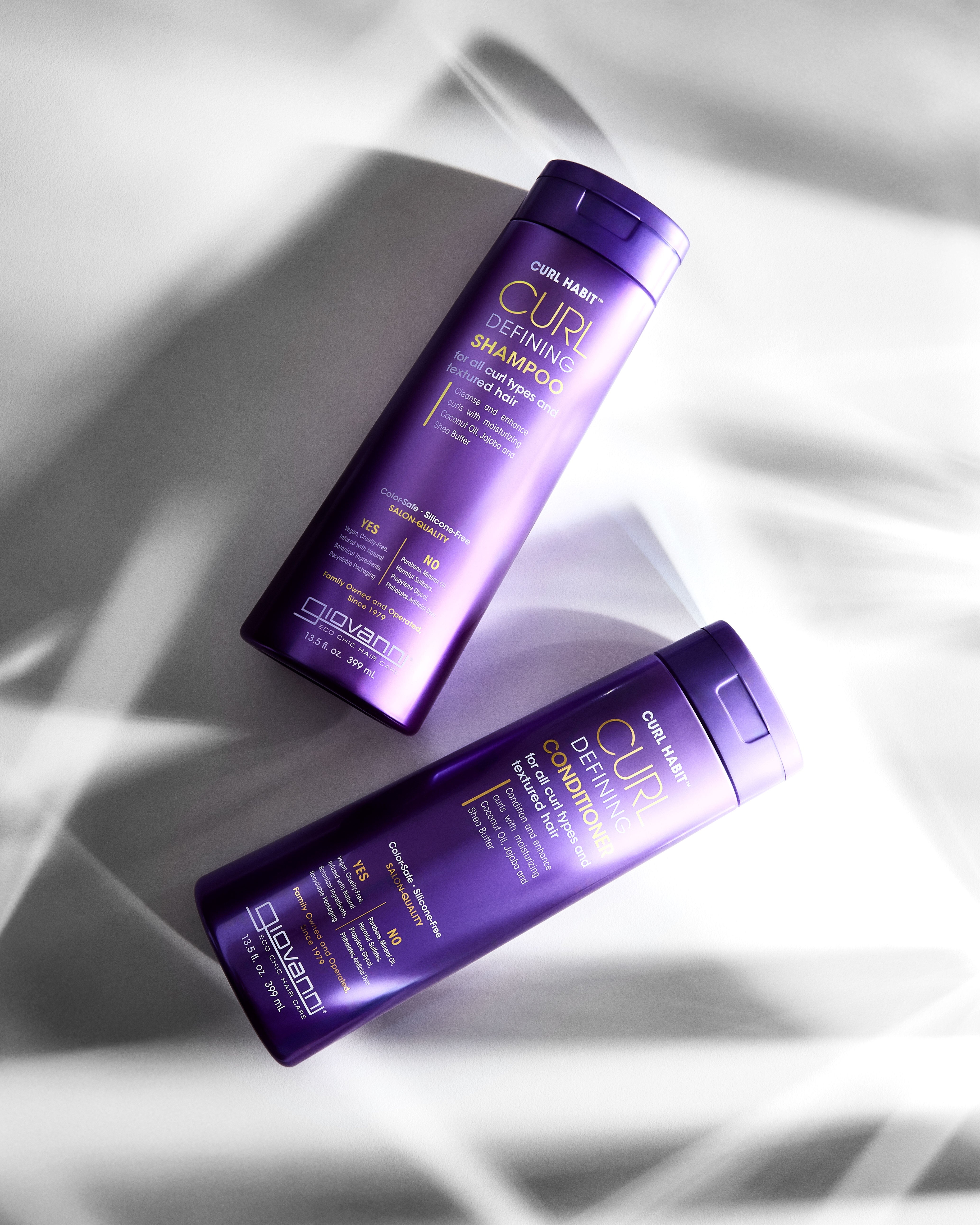 Two bottles of Giovanni CURL Habit Shampoo and Conditioner on a textured white background