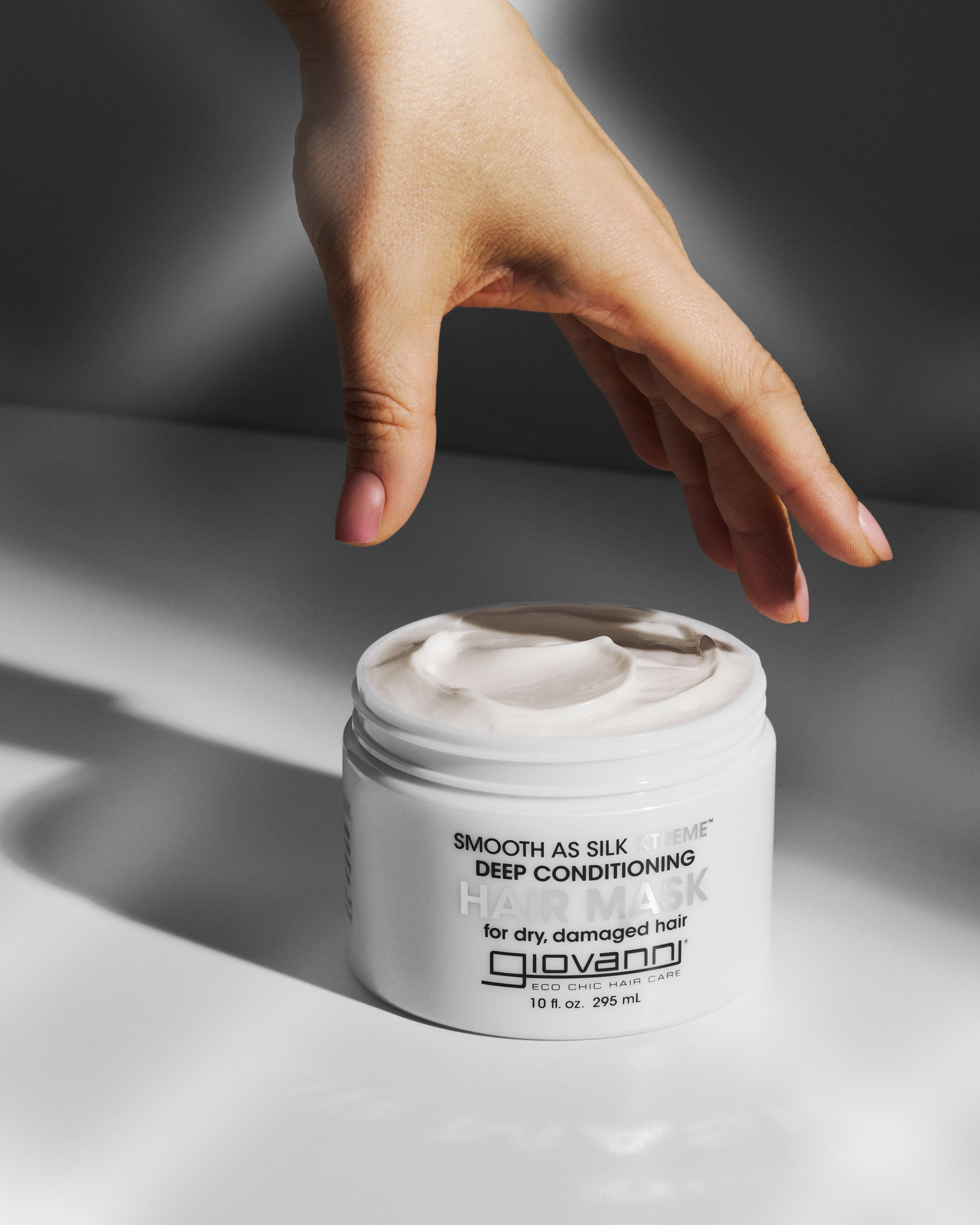 Hand reaching towards a jar of Giovanni Smooth as Silk Extreme Deep Conditioning Hair Mask product