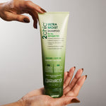 Hand holding a bottle of Giovanni 2Chic Ultra Moist Shampoo against a gray background