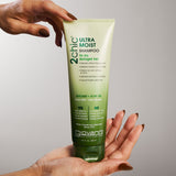 Hand holding a bottle of Giovanni 2Chic Ultra Moist Shampoo against a gray background