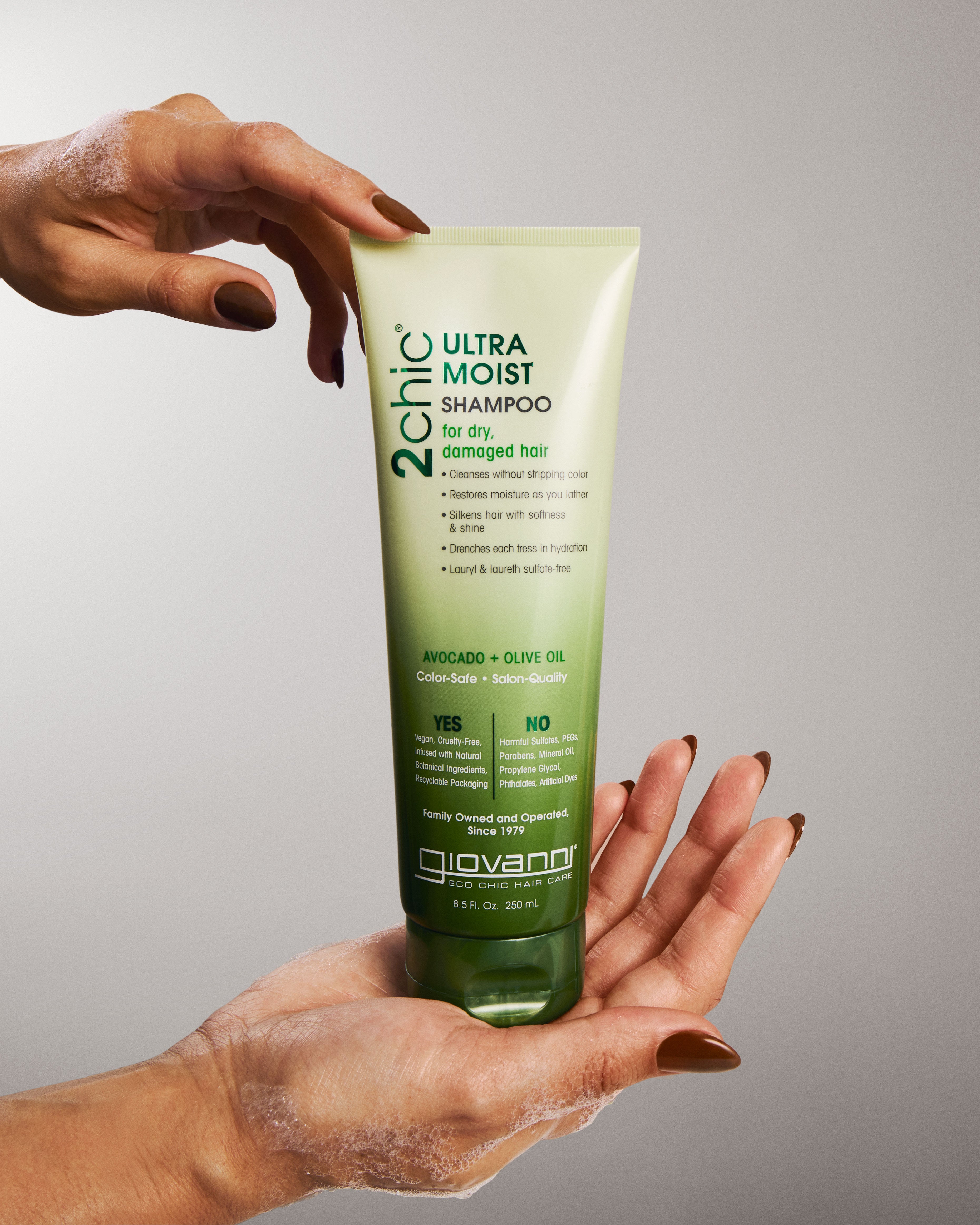 Hand holding a bottle of Giovanni 2Chic Ultra Moist Shampoo against a gray background