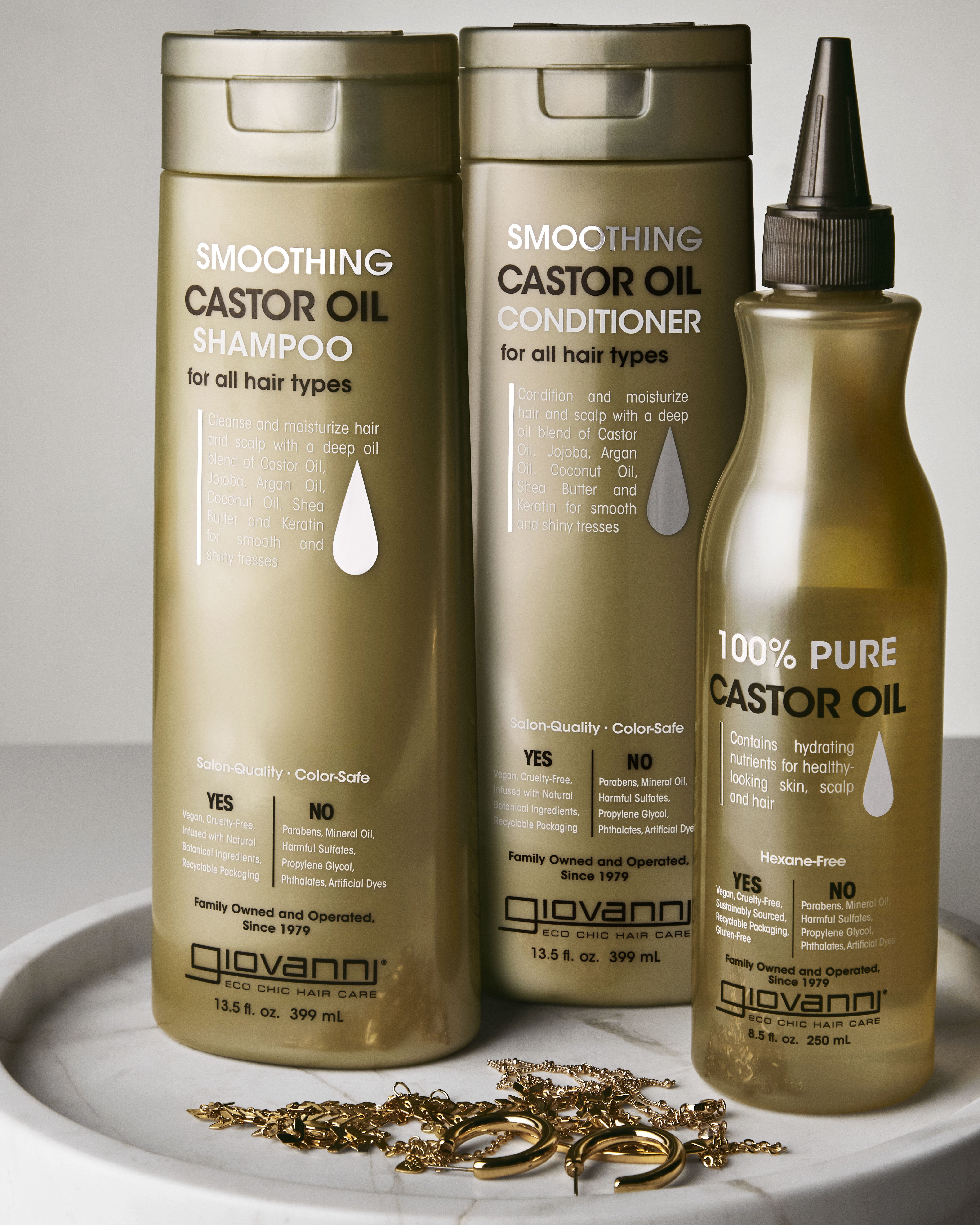 Giovanni Smoothing Castor Oil shampoo, conditioner, and oil on a white surface with gold jewelry.