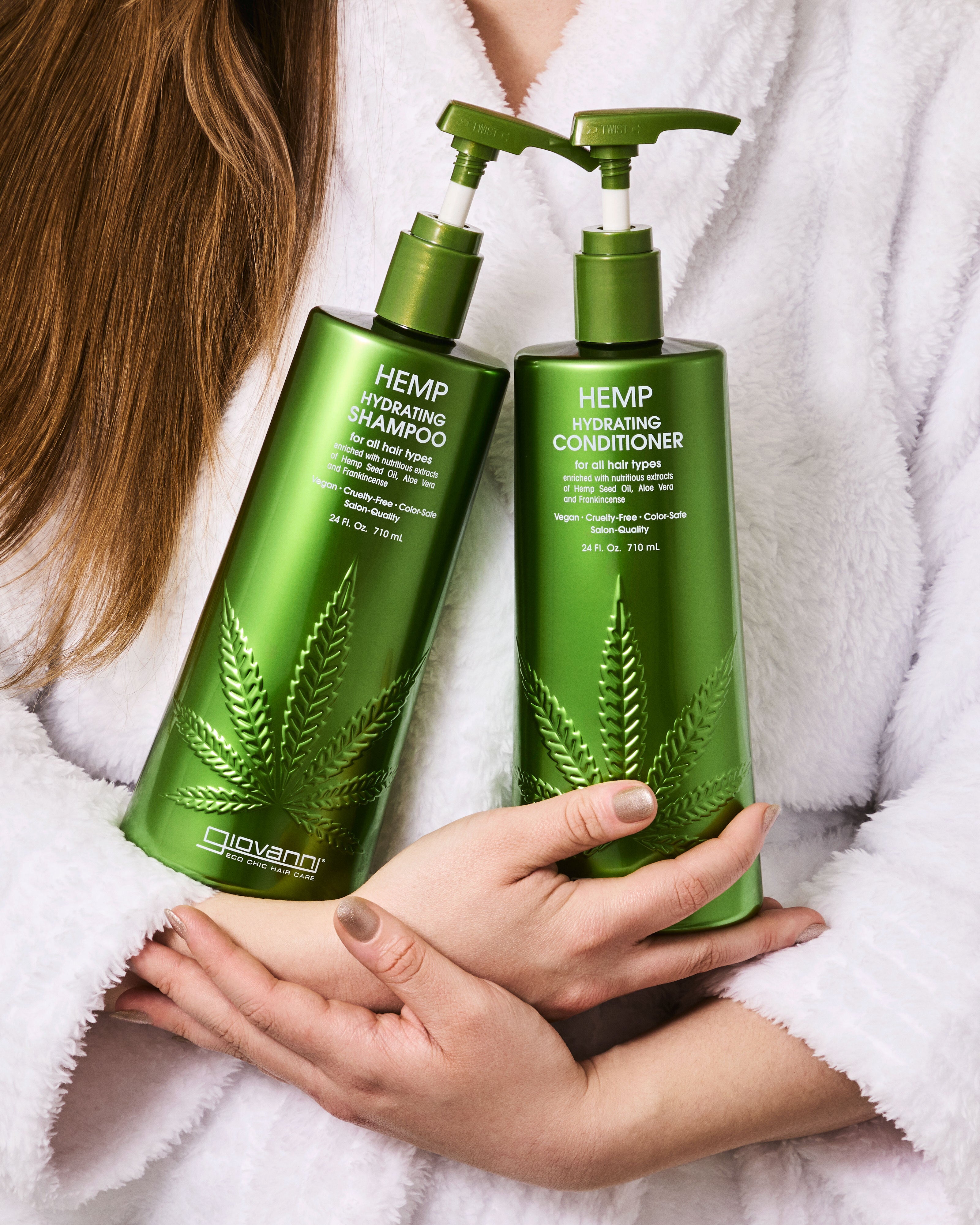 Two bottles of Giovanni Hemp Hydrating Shampoo and Conditioner held by a person in a white robe.