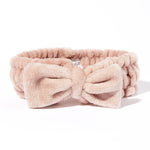 The Giovanni Cosmetics PLUSH MULTI-PURPOSE SPA HEADBAND (blush) is a soft, light pink headband with a large bow and non-slip elastic—ideal for keeping hair in place during your beauty routine, shown on a white background.